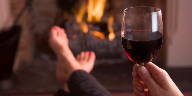 Feet warming at fireplace with hand holding wine