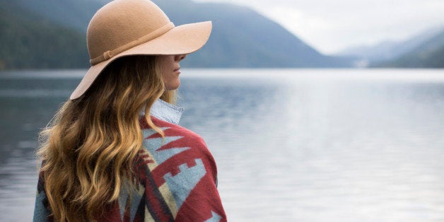 A woman with a floppy hat and native shall overlooking a lake.