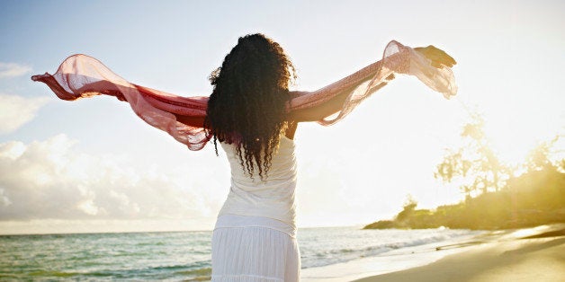 Woman on tropical beach at sunrise with arms outstretched towards sun