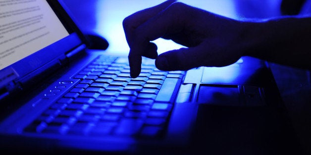 man's hand perched ready to type on notebook computer keyboard on conference table in Seattle office after work hours, with blue toned glow