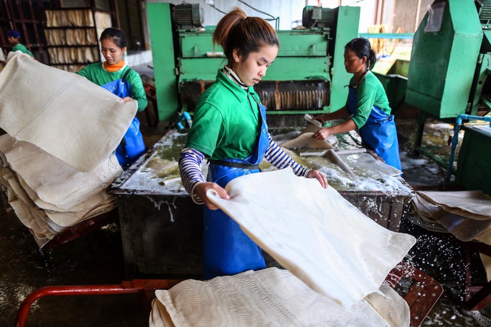 Workers handle rubber sheets as they pass through a rubber sheet washing machine at the Thai Hua Rubber Pcl factory in Samnuk