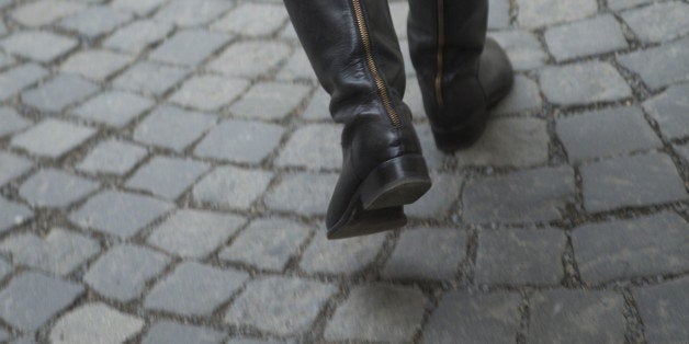 Rear view of woman's knee-high boots as she walks across stone courtyard in Prague.