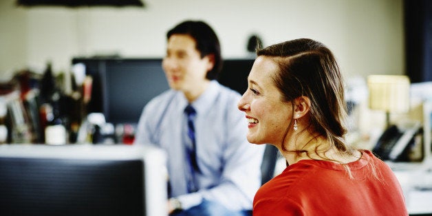 Smiling businesswoman in discussion with coworker at workstation in office