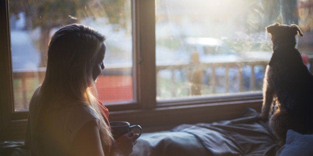 Girl watching dog with her cup of coffee by window