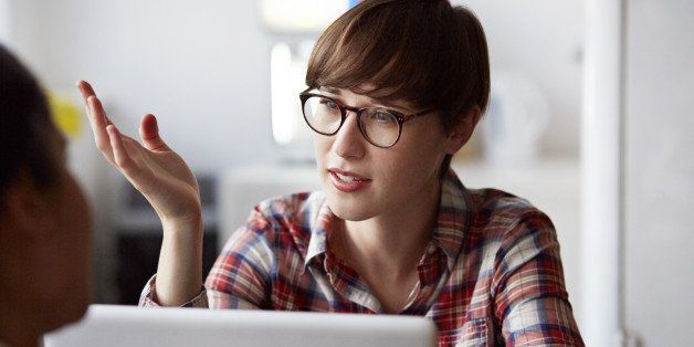 Creative businesswoman sitting by laptop, explaining to coworker