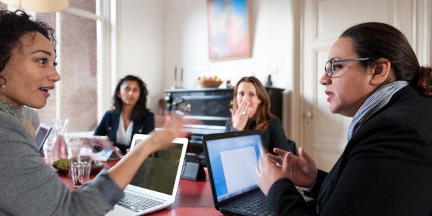 Woman interrupting another woman during a meeting. Two other women listening and one is responding startled.