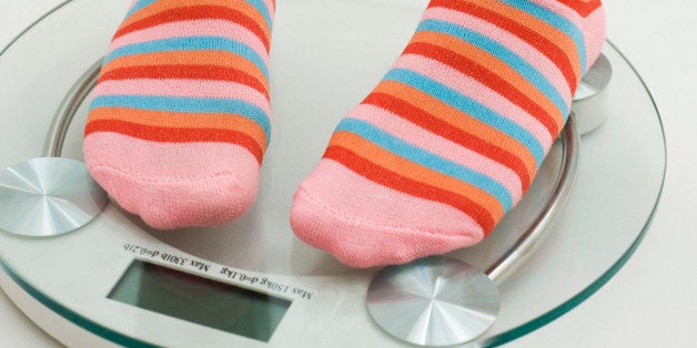 Girl weighing self on bathroom scale, cropped