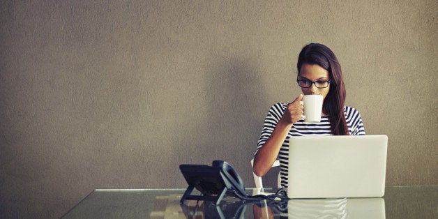 An attractive young businesswoman having coffee while working at her office desk