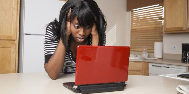 A young african american teen working on a netbook in the kitchen is disappointed at what she finds.