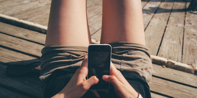 A girl texting on an iPhone on a dock.