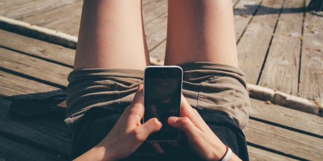 A girl texting on an iPhone on a dock.