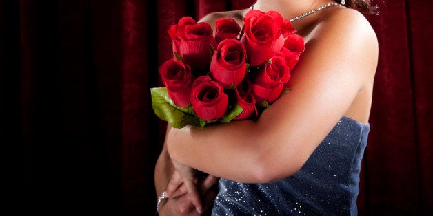 Photo of a beautiful young woman with dazzling smile and an armful of artificial roses, standing in the spotlight in front of a red curtain.