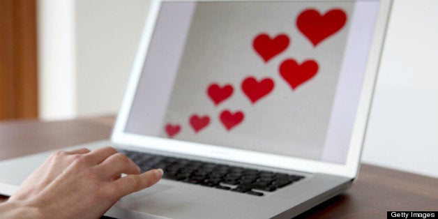 A woman's hand on a laptop keyboard with red hearts on the screen.