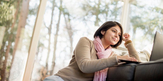 Woman sitting on the floor in front of a sofa looking at her laptop.