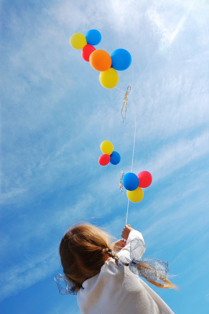 child flying colorful balloons in the blue sky