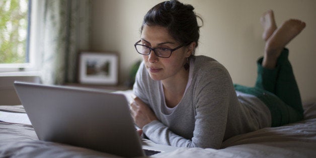 Young woman lying on bed and looking at a laptop.