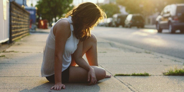 A girl sits on the sidewalk at sunset in Long Beach, NY.