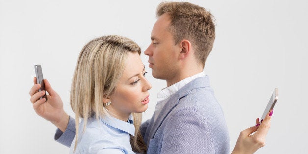 Young couple embracing and still using their mobile phones.