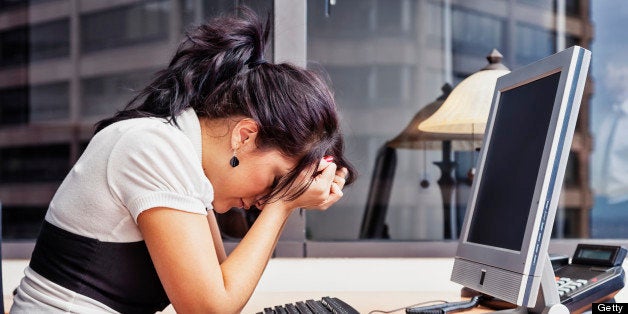 Photo of a businesswoman sitting at her desk with her head in her hands, as if having a very bad day.