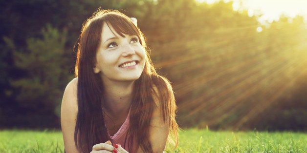 Young pretty woman lying on the grass at summer sunset. Natural happiness, fun and harmony.