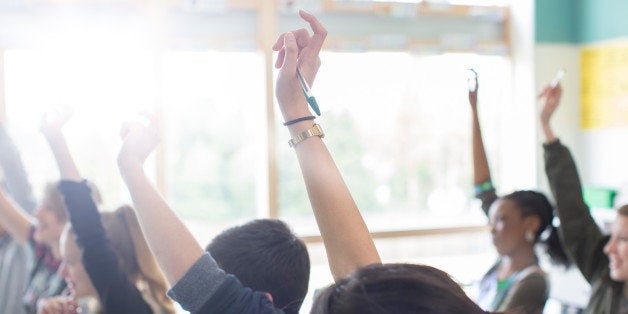 Teenage students with arms raised in classroom