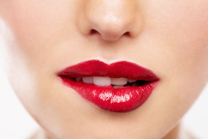 Cropped closeup of a woman wearing red lipstick and biting her lip