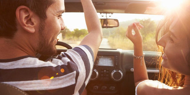 Young Couple Driving Along Country Road In Open Top Car