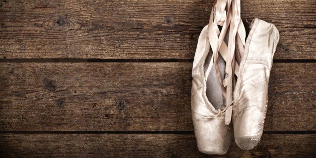 Old used pink ballet shoes hanging on wooden background