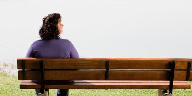 rear view of overweight woman sitting on park bench near lake
