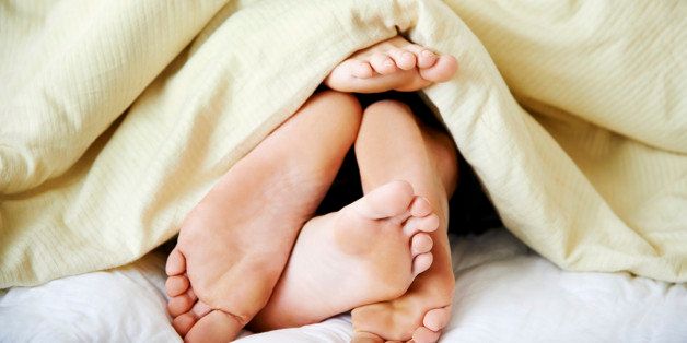 Cropped shot of a couple's feet poking out from under the bedsheets