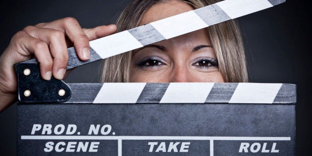 Pretty young woman holding a clapper over black background.