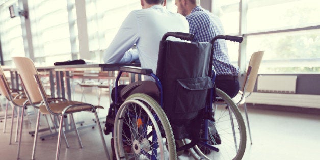 Disabled businessman sitting in a wheelchair at the conference table in board room and working with his colleague together. Back view, unrecognizable people. 