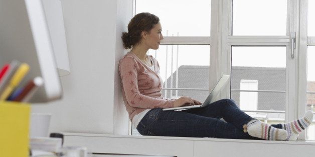 Woman sitting on windowsill using laptop
