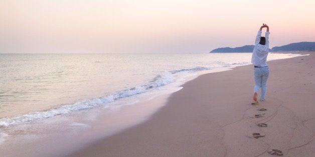 Landscape image of a Japanese woman stretches out her hands while walking on a beach in dawn. This image was taken in April 2015, Shimane Prefecture, Japan.