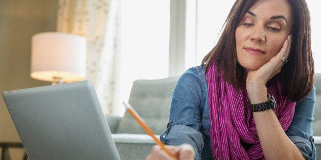 Mature woman with laptop writing in book at table