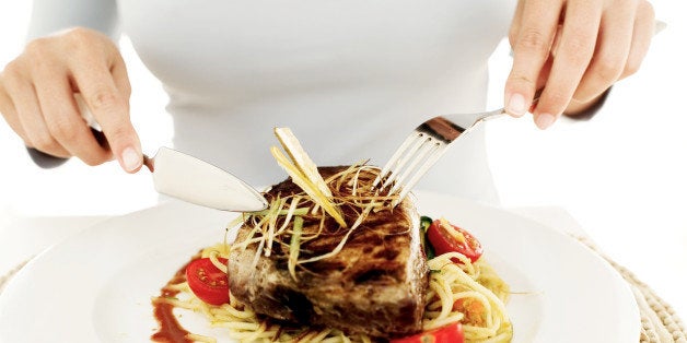 close-up of a woman's hands cutting a piece of food from a meal