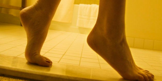 Bare legs and feet of woman standing on tiptoe in bathroom.