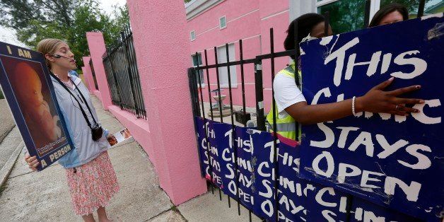 In this April 15, 2013 photo, abortion opponent Corrie Zastrow, left, calls out to patients while clinic escorts secure signs on the front gates to prevent the abortion opponents from visually confronting patients as they enter the Jackson Women's Health Organization clinic in Jackson, Miss. A federal judge on Monday temporarily blocked Mississippi from revoking the license of the state's only abortion clinic, saying the state cannot close the clinic while it still has a federal lawsuit pending to challenge the 2012 law. A trial date has not been set. (AP Photo/Rogelio V. Solis)