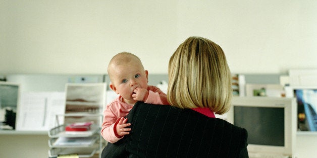 Woman working at desk holding baby girl (9-12 months), rear view