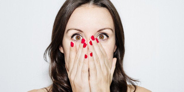 Surprise or fear face with beautiful eyes wide open. Portrait of a woman with brown and wavy hair on a white background.