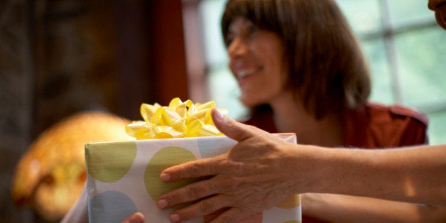 Two women exchanging gift over table, close-up of hands, out of focus woman in background