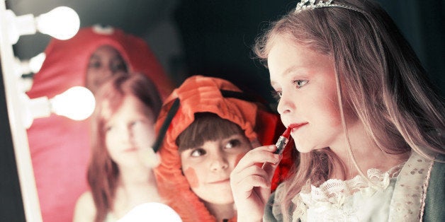 Two girls (5-8), one watching friend applying lipstick in stage mirror