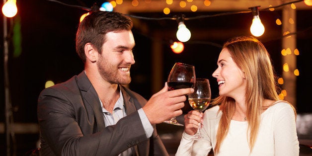 Couple eating dinner at rooftop restuarant holding glasses of wine