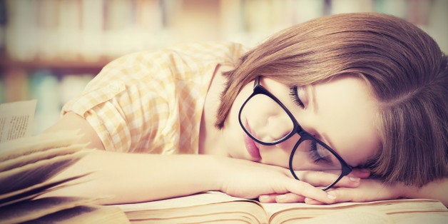 tired student girl with glasses sleeping on the books in the library