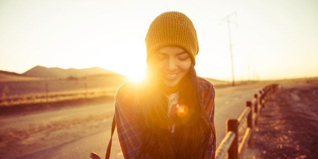 young woman sitting on fence post at sunset