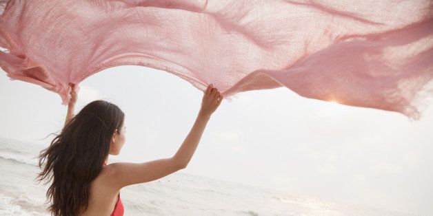 Young women on the beach holding scarf in the air and looking into the distance