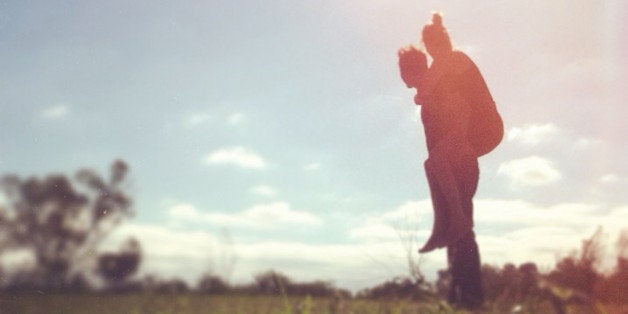 a couple standing with the female on the mans back in a field with the sun creating them in silhouette