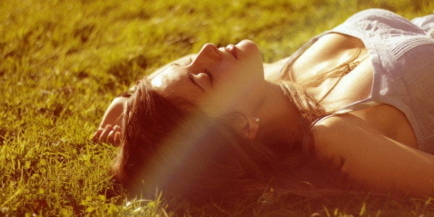 Girl enjoys sun, there's a warm summer mood around she is lying on grass.