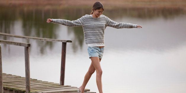 Woman walking on dock over lake with arms outstretched
