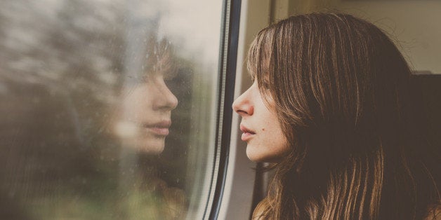 Woman looking through a window in a train with reflection.